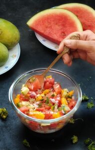 A bowl of Watermelon Mango Pico de Gallo next to mangoes and watermelon slices 