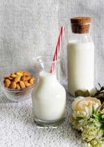 2 ingredient Homemade Almond milk Recipe served in glass bottle with red straw and almonds in the bowl on side 