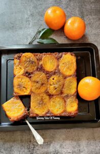 Orange-carrot Upside Down Cake placed on black tray with oranges on the side 